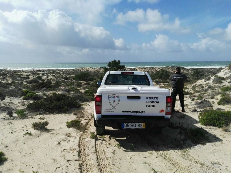 Vigilante da COPS junto a uma viatura da empresa, a observar a costa a partir das dunas