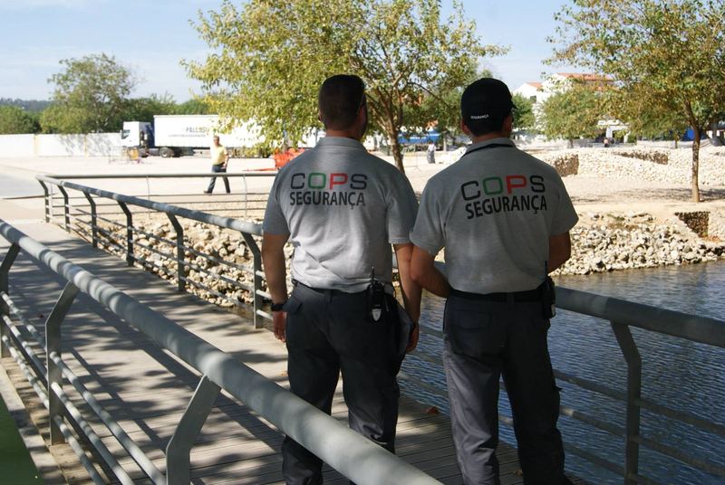Dois vigilantes da COPS fardados, em ronda num passadiço junto à água